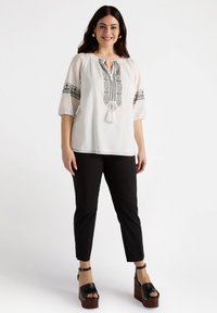 White blouse with black embroidered neckline and puffed sleeves, paired with black pants and black platform sandals, featuring a chunky wooden sole.