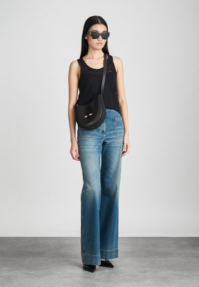 Melna bezdelīga topiņš ar mazu logotipu, platai zilas džinsa bikses, melna pleca soma ar zelta akcentiem un stūrainas melnas saulesbrilles.