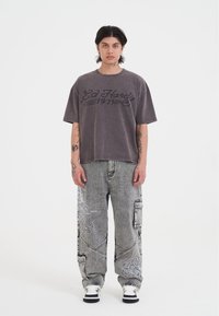 Gray oversized T-shirt with black "Ed Hardy 1971" text, paired with gray patterned cargo pants and black-and-white sneakers.