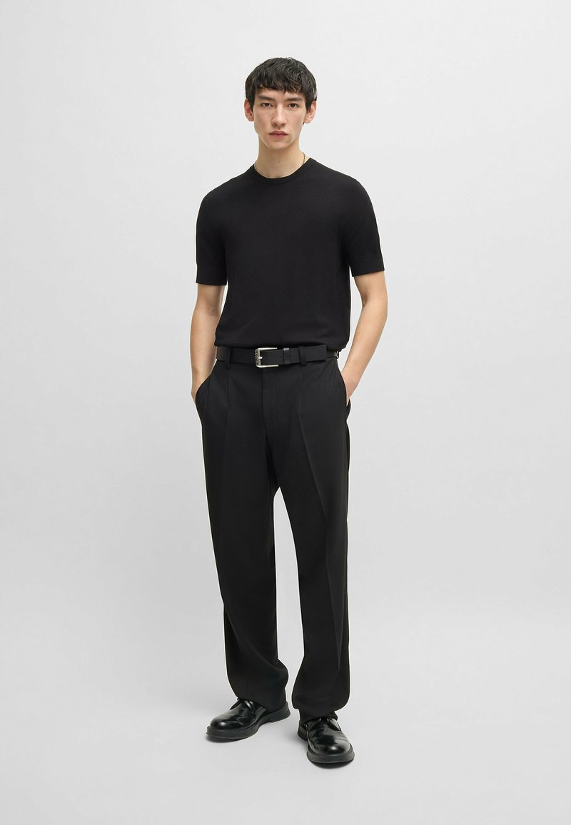 Black short-sleeve knit top paired with black tailored trousers and black lace-up shoes. Smooth texture, classic cut, and neutral color palette.