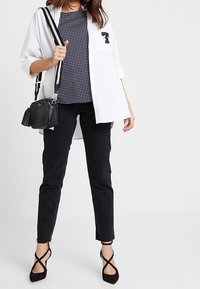 Bílé oversized tričko přes tmavě modré top se vzorem teček, doplněné černými skinny džínami a černými podpatky s křížovými pásky. Černá crossbody taška.