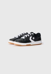 Sorte lærersneakers med hvite snørebånd og stjernelogo, med en kontrasterende hvit stripe og såle i gummigummi. Lavprofildesign.