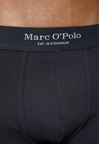 Boxer shorts noirs côtelés avec une large ceinture portant le texte blanc "Marc O'Polo EST. À STOCKHOLM". Texture lisse, design ajusté.