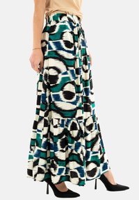 Gonna maxi con un audace motivo astratto in nero, verde petrolio e bianco, dotata di un orlo arruffato e una cintura elastica. Indossata con tacchi neri.