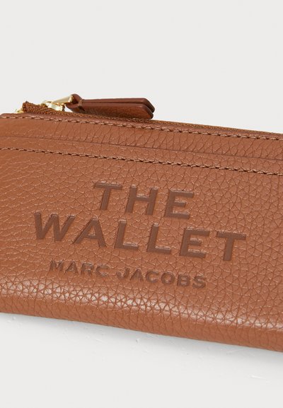 Cartera de cuero texturizado marrón con el texto en relieve "THE WALLET" y "MARC JACOBS." Presenta un cierre con cremallera y herrajes en tono dorado.