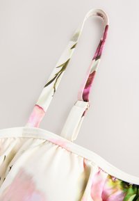 Bretelle fine réglable avec curseur en métal sur tissu crème à motifs floraux, partie d'un vêtement léger.