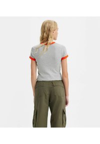 Camiseta gris de manga corta con puños acanalados naranjas, combinada con pantalones cargo verde olivo que tienen bolsillos laterales y un corte holgado.