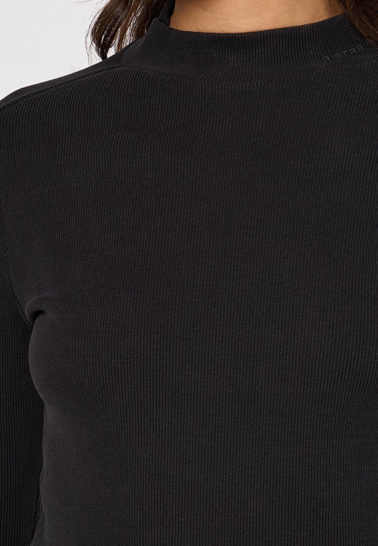 Haut noir à manches longues côtelé avec un col montant, un tissu texturé et une coupe ajustée, mettant en avant un design simple et épuré.