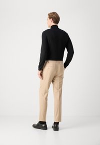 Černý top s dlouhým rukávem a vysokým límcem v kombinaci s béžovými elegantními kalhotami a černými botami. Kalhoty mají zadní kapsy a slim fit.