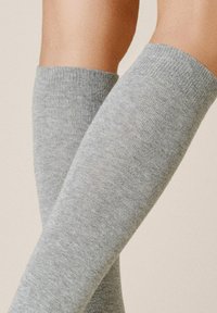 Graue kniehohe Socken mit einem gerippten Muster. Das Material wirkt weich und dehnbar, in einer einfarbigen Ausführung ohne Muster oder Akzente.