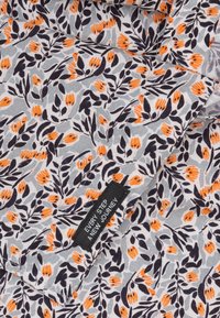 Patroonstof met kleine oranje bloemen en donkere bladeren op een lichtgrijze achtergrond. Bevat een zwart label met witte tekst.