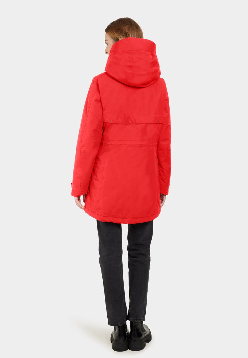 Chaqueta aislante roja con capucha, que presenta una textura suave, una cintura ajustada y puños ajustables, combinada con pantalones oscuros y botas.