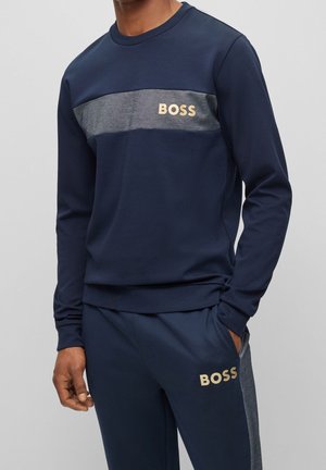 Sudadera navy con raya horizontal gris y logotipo dorado "BOSS" en el pecho. Tejido suave, mangas largas, puños y bajo acanalados.