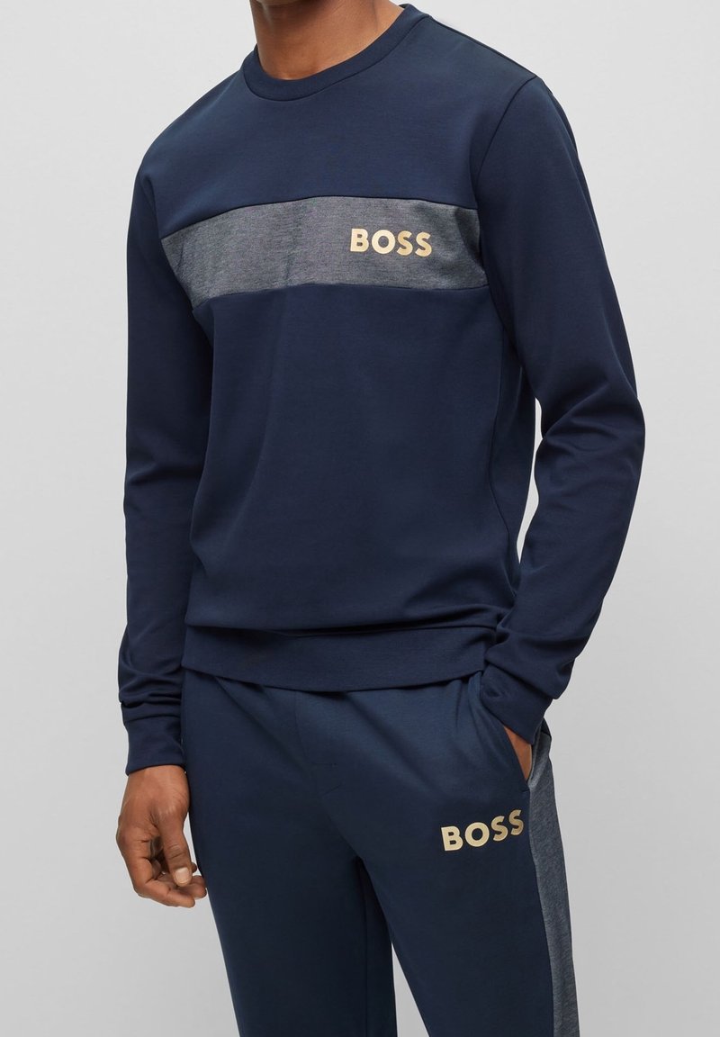 Marinblå sweatshirt med grå horisontell rand och guld "BOSS"-logotyp på bröstet. Mjuk kvalitet, långa ärmar, ribbade muddar och fåll.