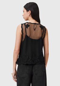Čierny top bez rukávov s priehľadným chrbtom, kvetinovou výšivkou pozdĺž lemu a otvorom v tvare kľúčovej dierky na krku. Jemná tkanina a textúrované doplnky.