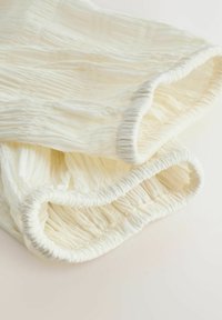 Lys cremefarvet stof med tekstureret rynkning og elastiske kanter. Blødt, let materiale, der falder blødt med subtile variationer.