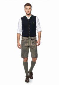 Traditionelles bayerisches Outfit mit einer dunkelblauen Weste mit grünen Akzenten, grauen Lederhosen, knielangen grünen Socken und dunkelbraunen Schuhen.
