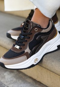 Hnědé a černé tenisky sítě, hadí textura a kovové akcenty. Design zahrnuje polstrovaný límec a kontrastní podrážku.