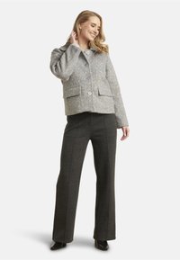 Gray wool blend jacket with a textured finish, featuring a collared neckline, front buttons, and two chest pockets, paired with dark tailored pants.