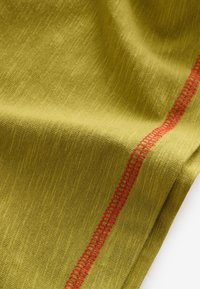 Green fabric with a textured surface and a red decorative stitch running along one edge. The material appears soft and lightweight.