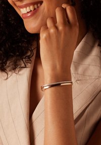 Roze gouden metalen armband met een strak ontwerp, voorzien van een rechte band en een rij kleine heldere stenen langs de bovenrand.