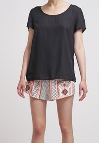 Donna che indossa una maglietta nera a maniche corte, larga, e pantaloni corti con un motivo geometrico nei colori arancione, nero e bianco.