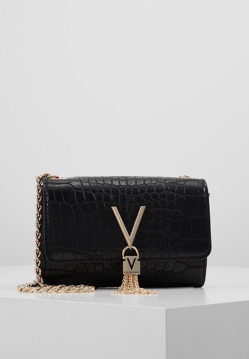 Black crocodile-patterned leather handbag with a gold chain strap. Features a prominent gold logo clasp with a tassel detail.