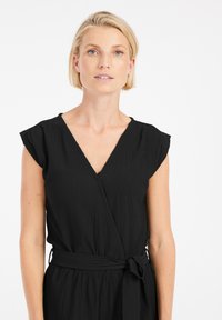 Zwarte wikkeljurk met korte gefruite mouwen, een diepe V-hals, gestructureerde stof en een bijpassende strikceintuur op de taille.