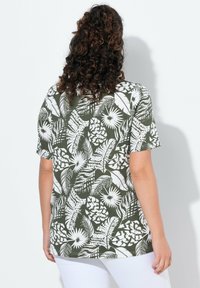 Zelená košile s krátkým rukávem s bílými tropickými vzory, volný střih a mírně zakřivený lem, vyrobená z lehkého materiálu.