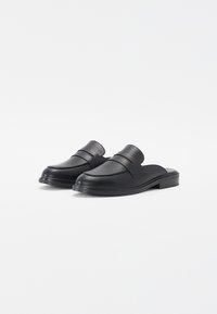 Black leather slip-on shoes with a smooth finish, rounded toe, and minimalistic strap detail across the upper. Flat sole, compact design.