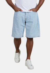 Pantalones cortos de mezclilla azul claro con un diseño de pierna recta, bolsillos frontales y un fit relajado, combinados con zapatillas blancas.