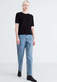 Black short-sleeve knit top paired with light blue relaxed-fit jeans and black pointed-toe ankle boots, standing on a plain background.