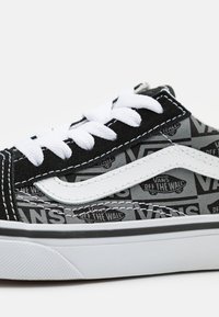 Zapatilla de skate negra y gris con un patrón repetido del logo "VANS", cordones blancos y una característica franja lateral blanca con una suela de goma.