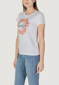 Weißes Baumwoll-T-Shirt mit orangefarbenem Blumenmuster und dem Wort "LiUJo" in Schwarz, runder Ausschnitt, kurze Ärmel und taillierte Passform.