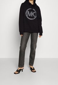 Black hoodie with a leopard-print logo, paired with gray jeans and black heeled sandals. Hoodie features drawstring and ribbed cuffs.