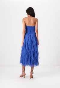 Blue strapless dress with ruffled tulle layers, knee-length, fitted bodice with ruching, worn with tan strappy heels.
