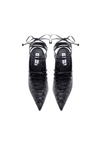 Μαύρα flats με μυτερή μύτη και δέσιμο με κορδόνια, με λουριά που τυλίγονται γύρω από τον αστράγαλο, εμφανιζόμενα από πάνω σε λευκό φόντο.