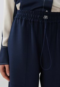 Navy blue joggers with an elastic waistband, featuring a drawstring detail and textured fabric. Side seam pockets are also visible.