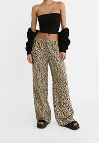 Pantalon large à imprimé léopard en beige et noir, associé à un haut bustier noir et des sandales compensées noires. Cardigan en maille texturée.