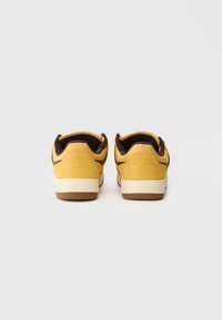 Dzeltenas zamšādas sporta kurpes ar brūnu gumijas zoli un akcentiem. Apaļa aizmugures konstrukcija ar mīkstu iekšējo oderi ērtībai.