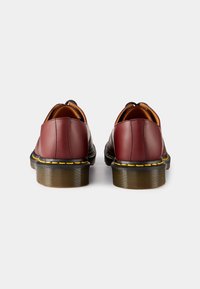 Bruine lederen schoenen met ronde achterkant, contrasterende gele stiksels en gestructureerde bruine zolen. Glad afwerking en slank ontwerp.