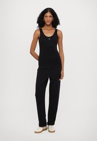 Top in cotone nero senza maniche, con scollo rotondo e piccolo logo, abbinato a pantaloni neri e sneakers color crema. Tessuto liscio, vestibilità casual.