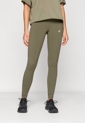 Olijfgroene active leggings met een getailleerd ontwerp en een gladde textuur, gecombineerd met een losse olijfkleurige top. Er worden zwarte sportschoenen gedragen.
