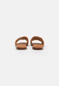 Brune flate sandaler med to lodne stroppar, ei glatt tan fotbed og ei lågprofil såle. Texturerte detaljar på stroppane gir ekstra stil.