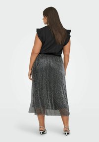 Top negro con mangas con volantes, combinado con una falda plisada gris brillante que presenta acentos metálicos. Sandalias plateadas completan el look.