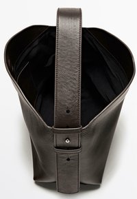 Tmavá kožená kabelka typu bucket s širokým otevřením, silným popruhem a minimálním prošitím. Vnitřek je vybaven černou podšívkou.