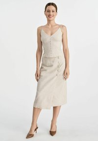 Jasno beżowa lniana koszulka na ramiączkach z guzikami, w połączeniu z dopasowaną spódnicą do kolan z rozcięciem z przodu i akcentami w postaci guzików. Brązowe szpilki w szpic.