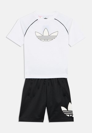 Wit kortärmelig mesh-top met zwarte biezen en Adidas-logo, gecombineerd met zwarte mesh-short met een groot Adidas-logo op het linkerbeen.