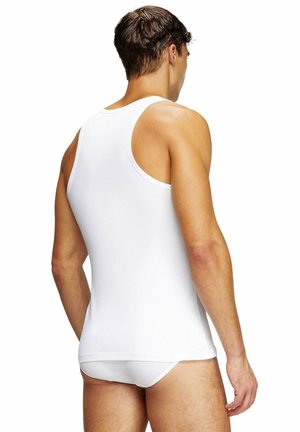 Man die een wit mouwloos hemd en witte slip draagt, gezien van achteren tegen een effen witte achtergrond.