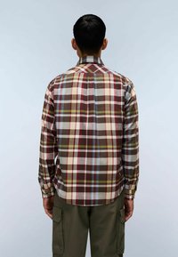 Uomo di spalle che indossa una camicia a maniche lunghe a quadri multicolori e pantaloni cargo verde oliva su uno sfondo chiaro e uniforme.